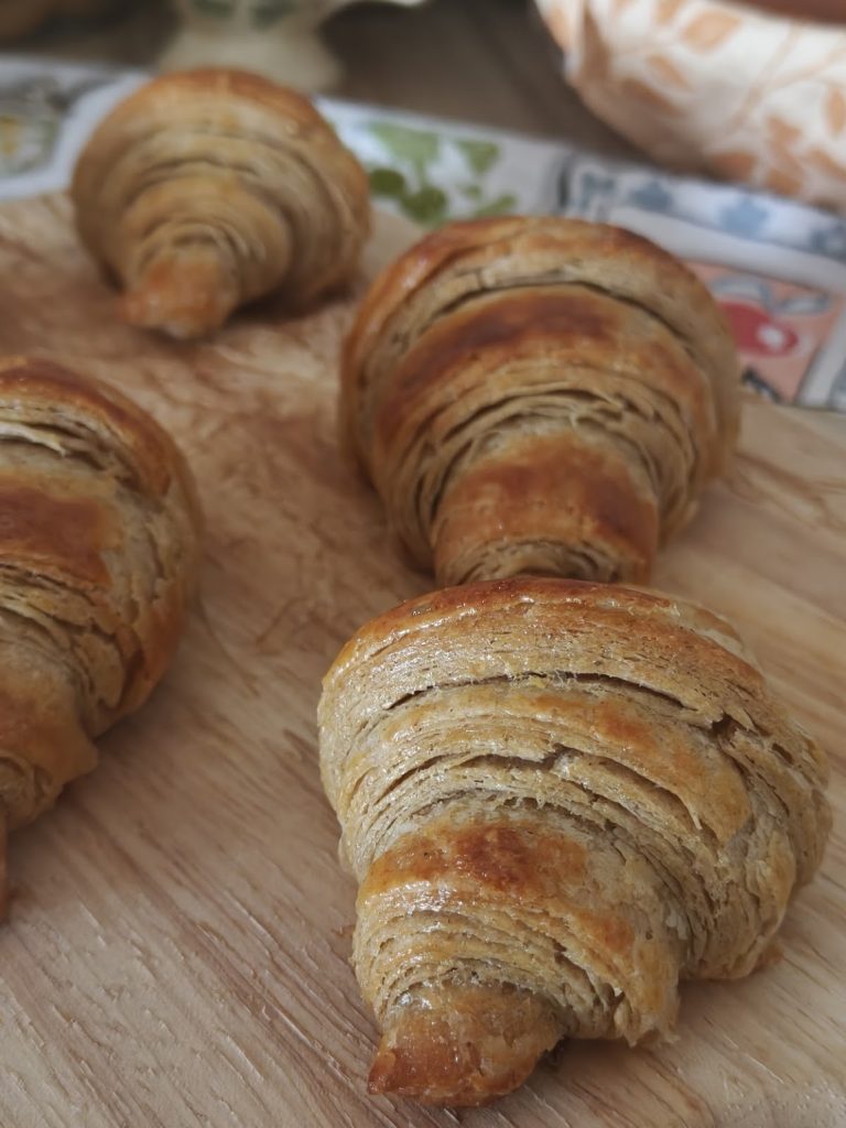 Rye and honey croissants on a wooden board, their layers open and flaky