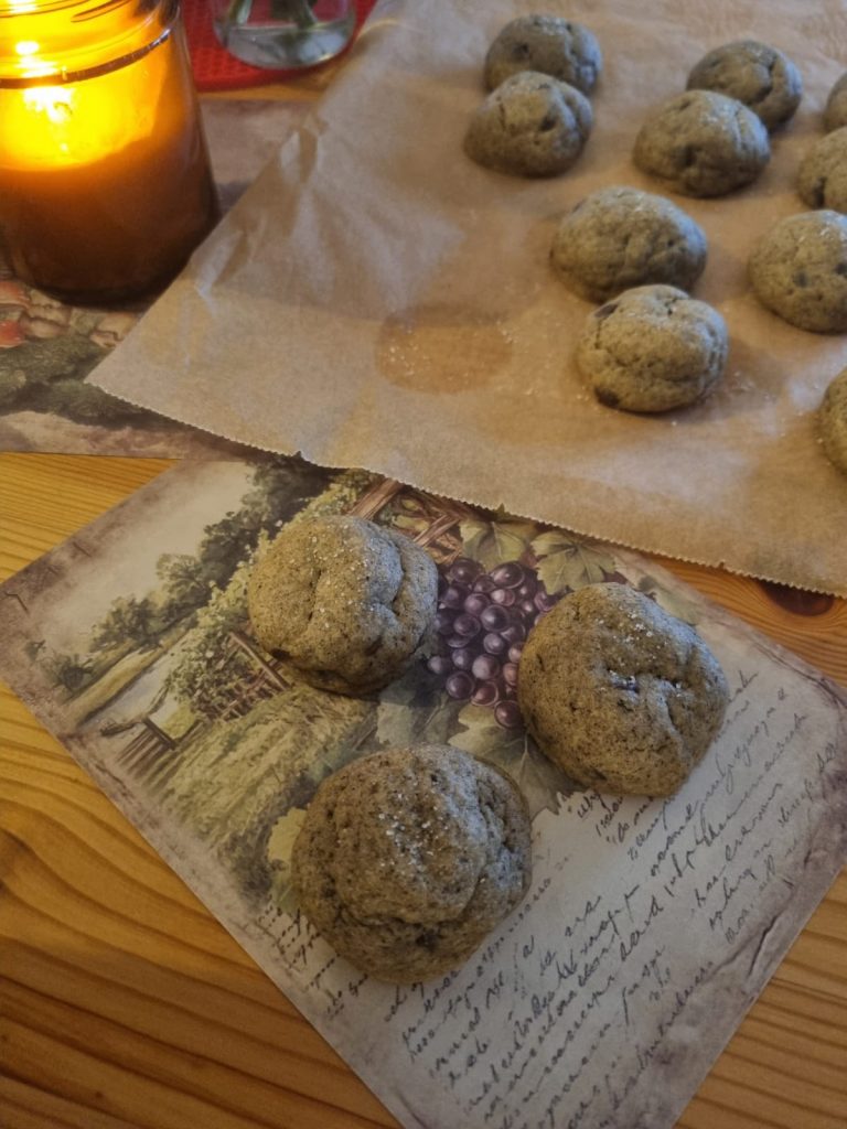 Baked brown cookies cooling on parchment, three set out on a vintage napkin beside a lit candle