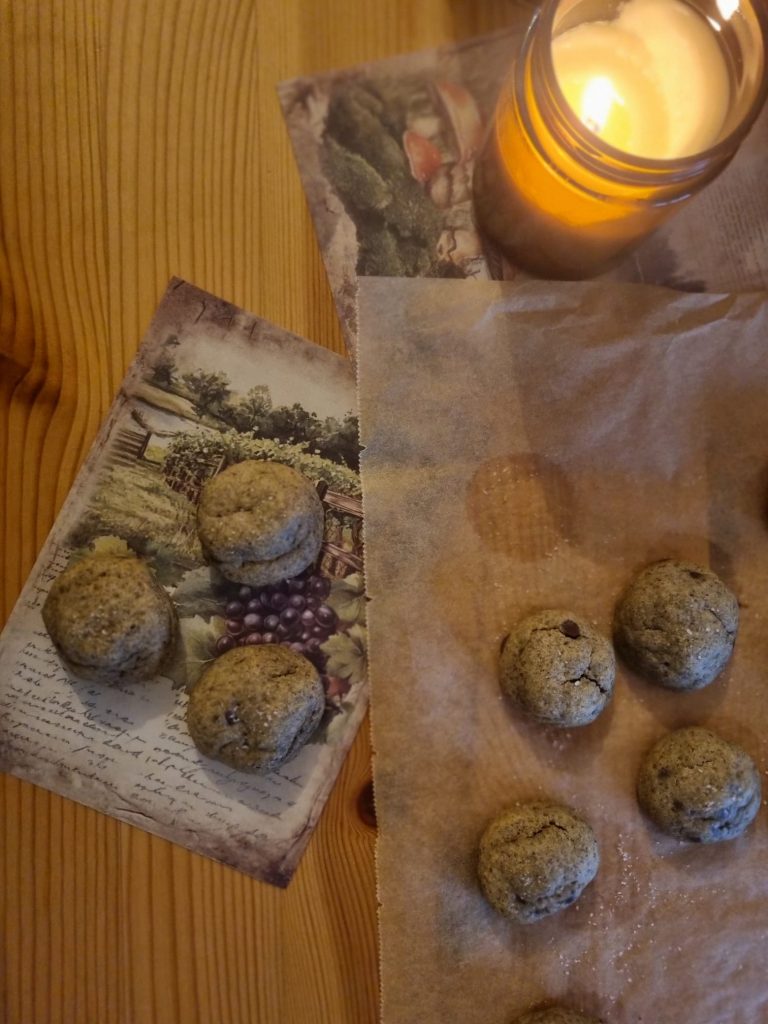 Brown cookies on baking parchment and vintage postcards, lit by a candle on a pine table