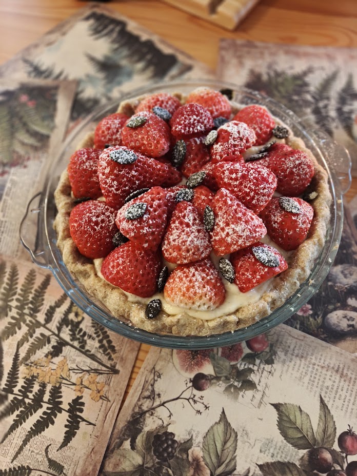 Strawberry tart in a glass dish, berries dusted with icing sugar over vanilla custard
